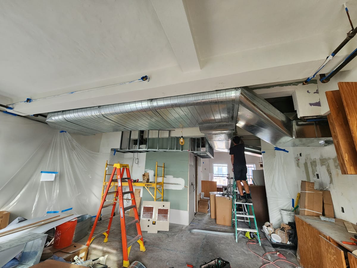 Technician installing large commercial ductwork from ladder